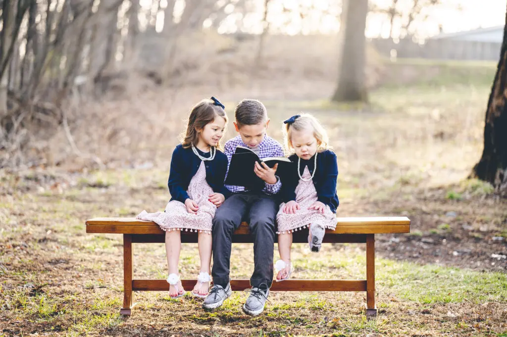 Scenic view of kids sitting on the bench and reading the bible